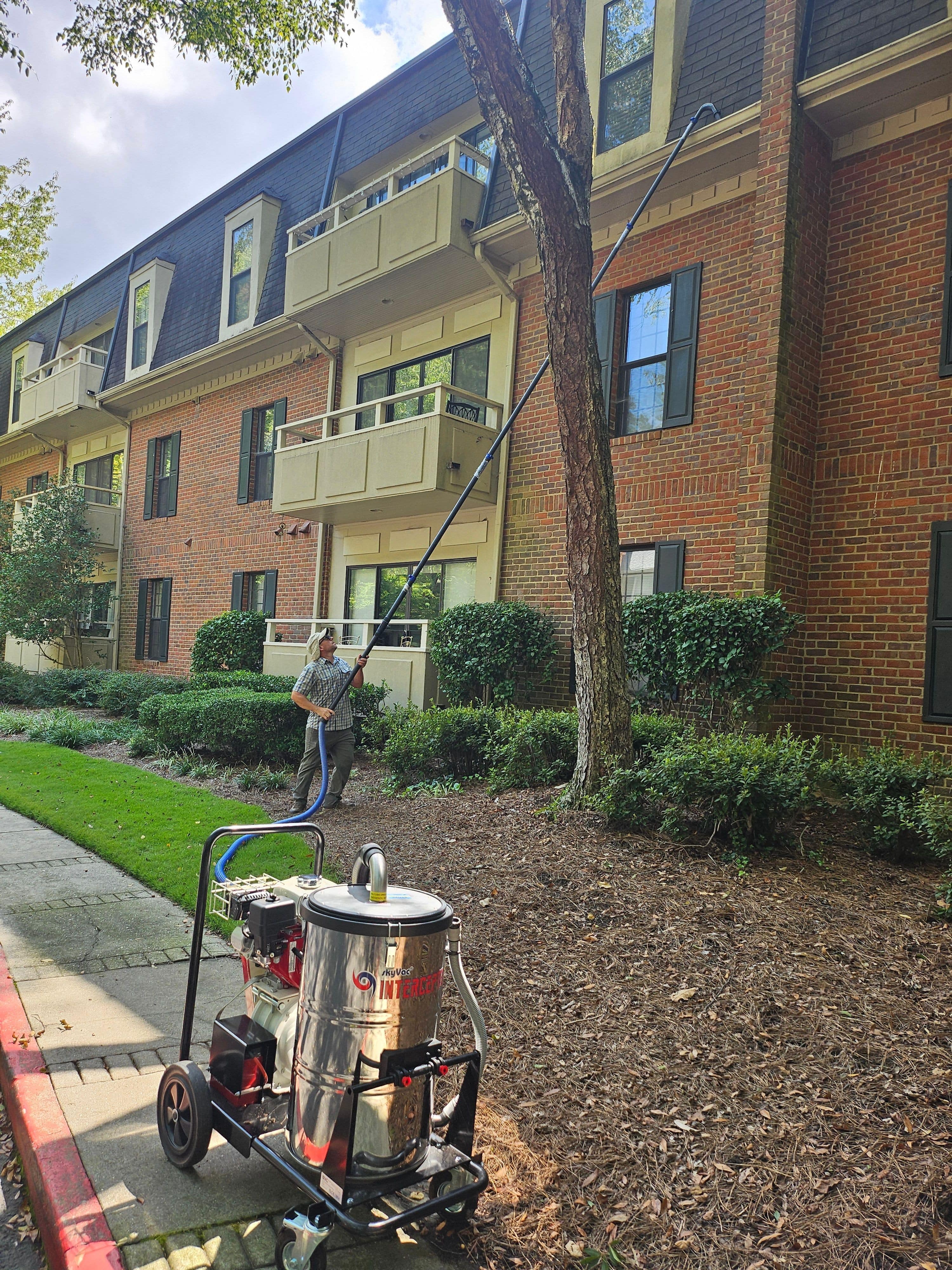 Photo of a Penson Pressure Washing team member using a gutter vacuum to safely clean gutters from the ground of an apartment building
