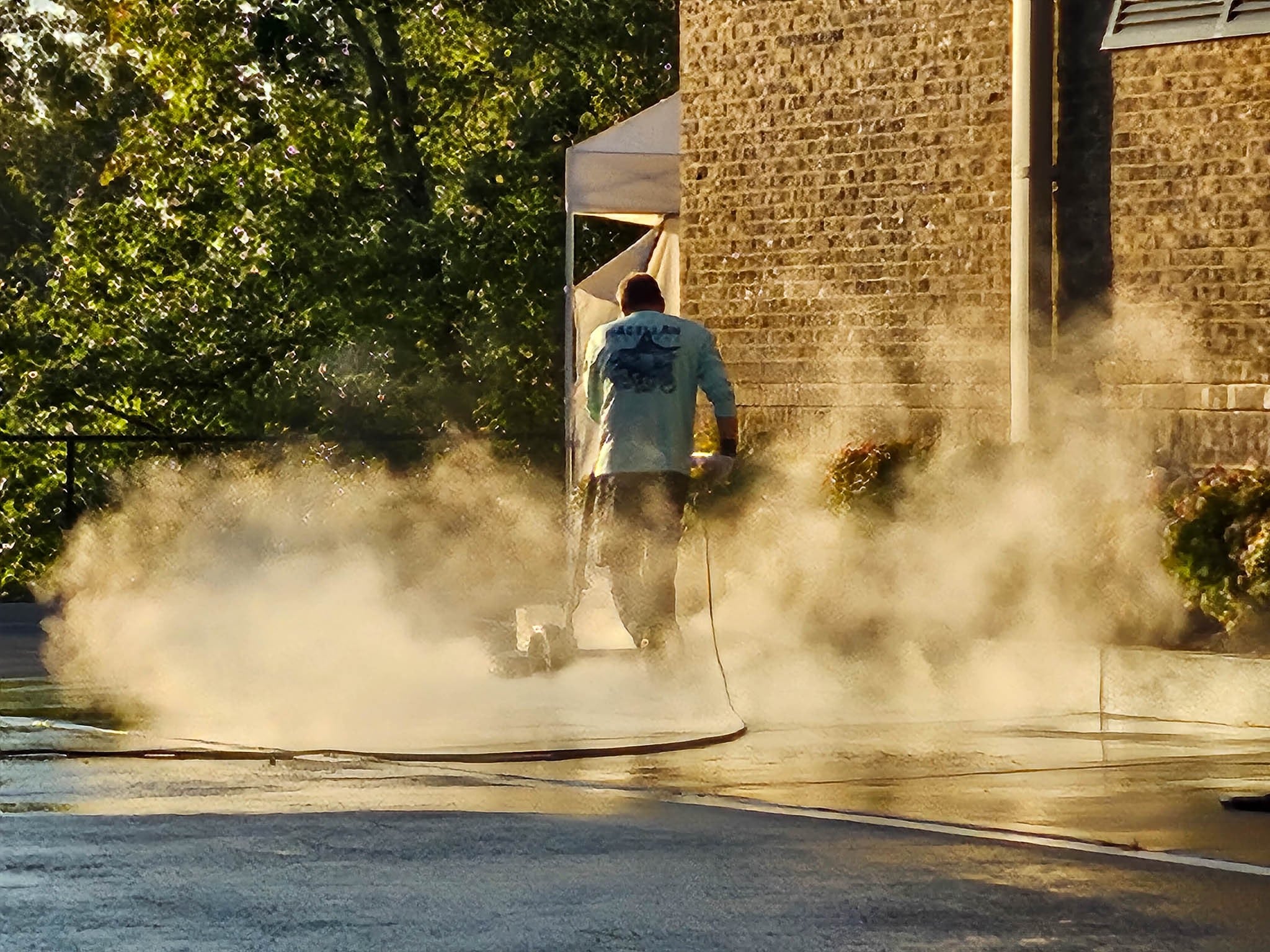 Penson Pressure Washing team member using rotary wash machine to clean concrete in parking lot of a commercial office building.