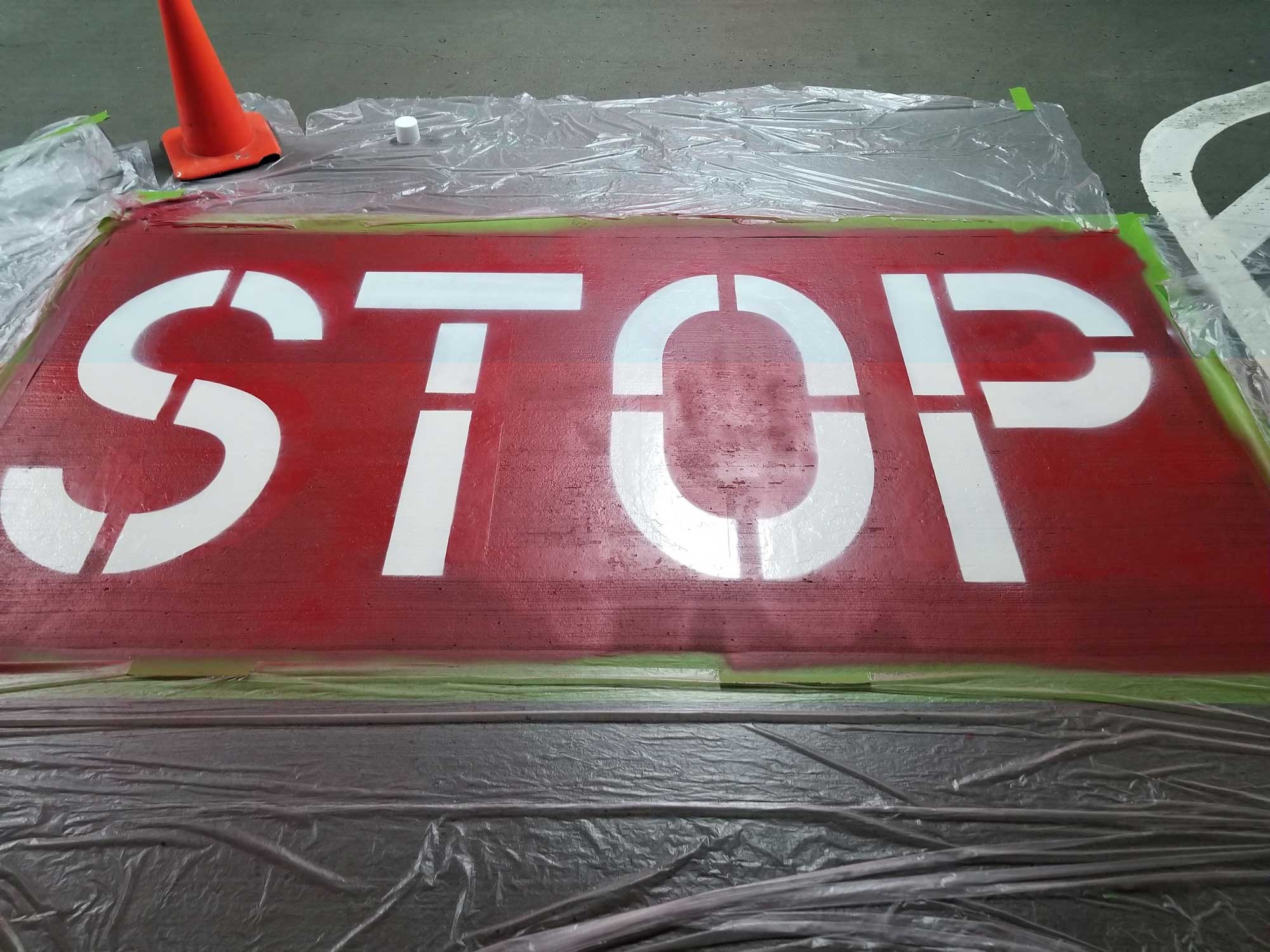 The word "stop" being stenciled and painted on a parking garage floor by Penson Pressure Washing team.